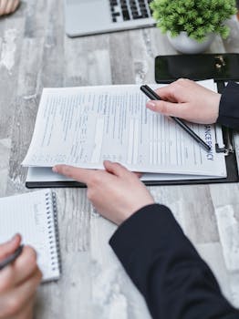 Close-up of hands analyzing insurance policy paperwork with pen on table.