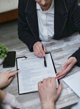 An agent and clients discussing paperwork for home insurance at a meeting table.