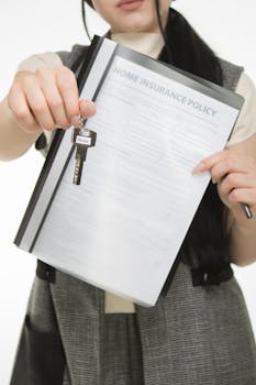 Close-up of person holding home insurance document and house key, symbolizing real estate and security.