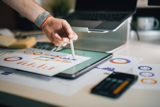 Hand using a tablet and charts on desk to analyze business data. Ideal for finance, business, and technology themes.